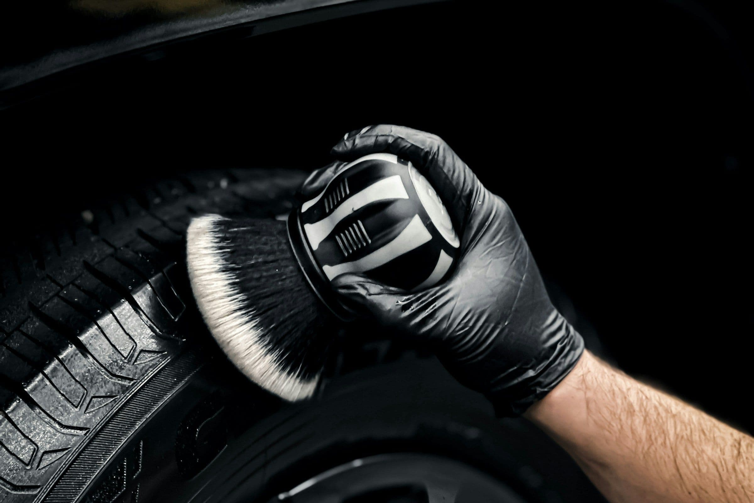 Gehandschoende hand reinigt een band met een detailingborstel