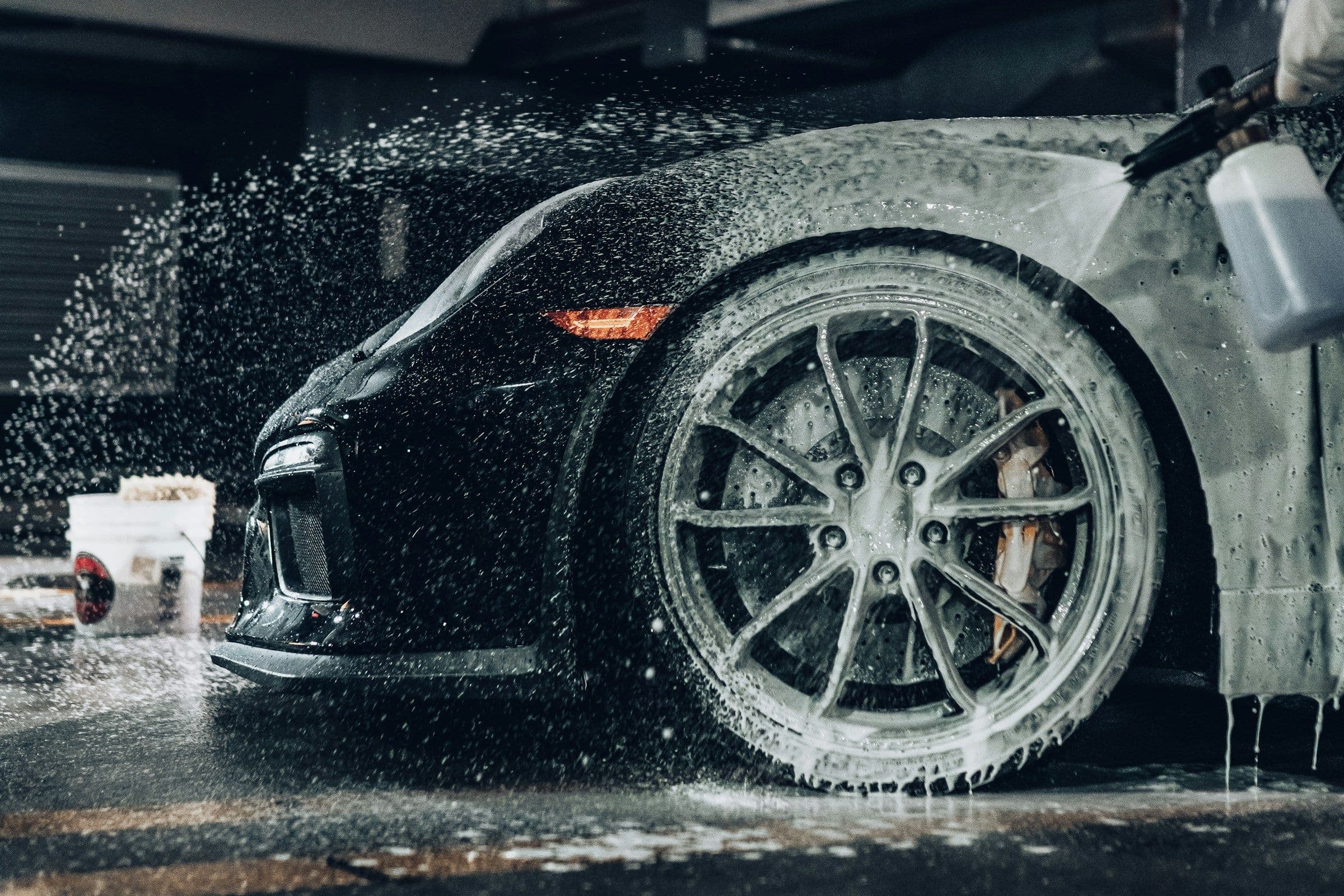 Zwarte sportwagen bedekt met snow foam tijdens een handwas